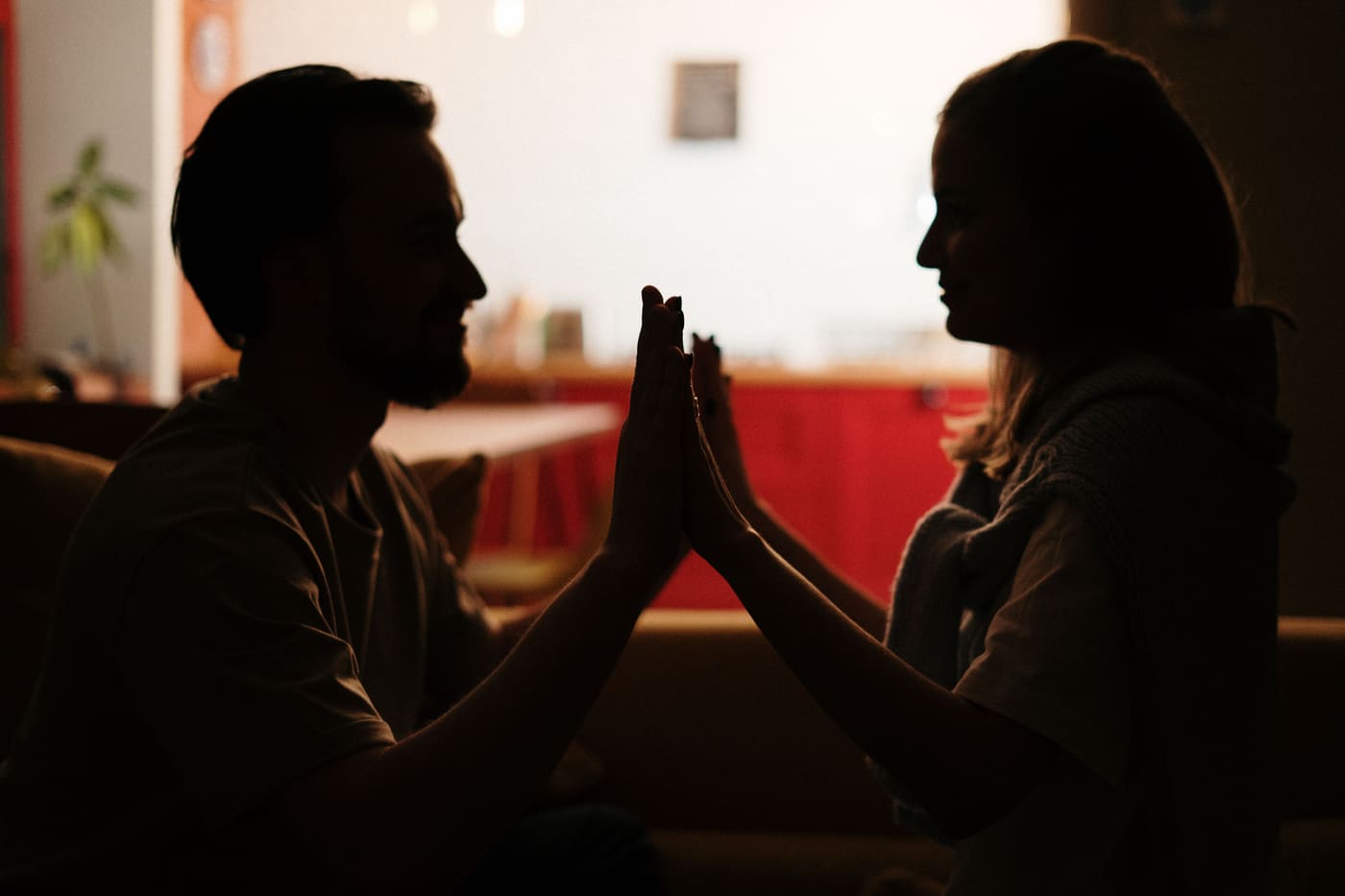 Silhouette of a couple reaching out to touch hands, playful moment on a couch