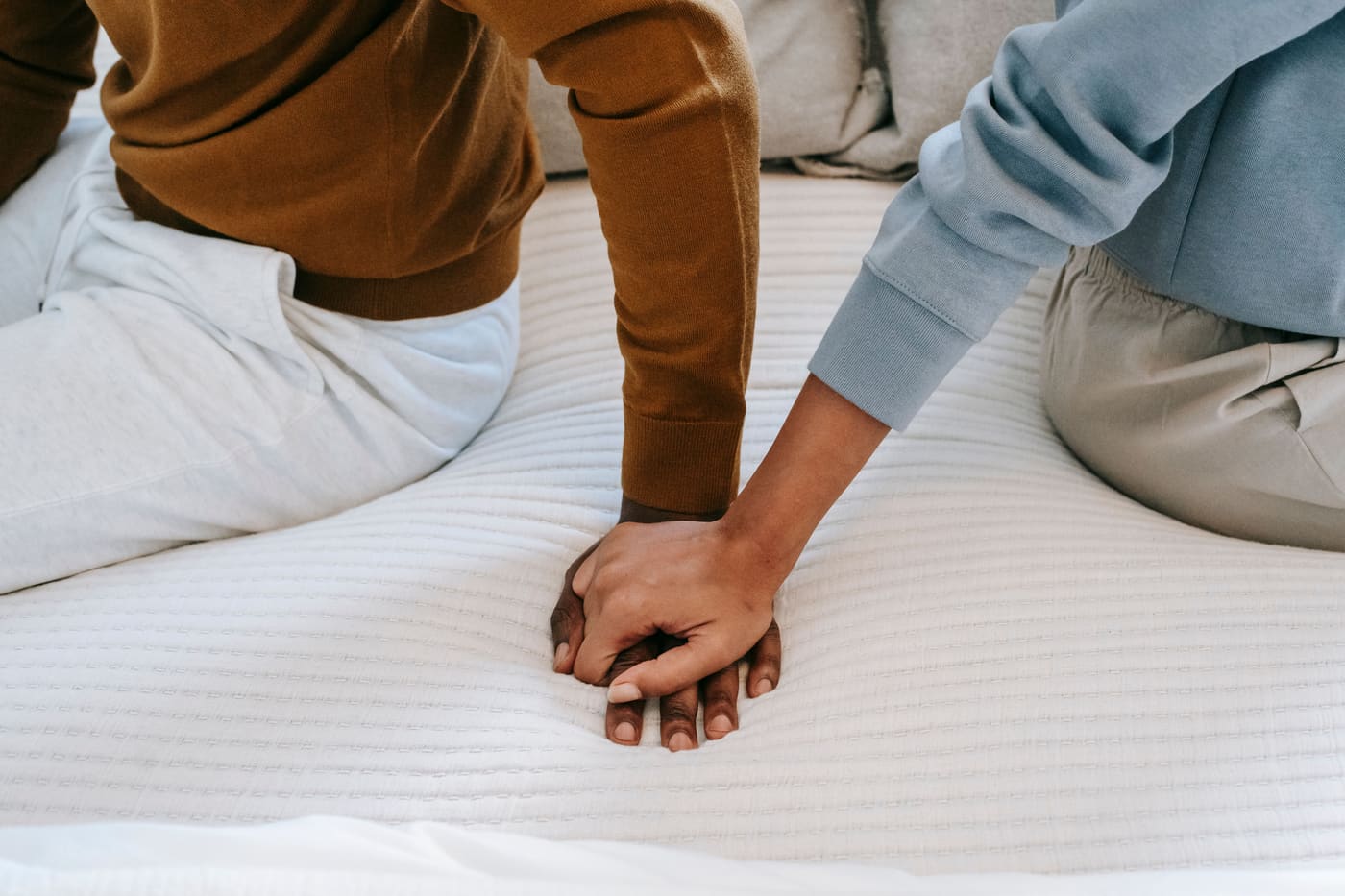 Close-up of a couple's hands touching on a bed, faces out of frame