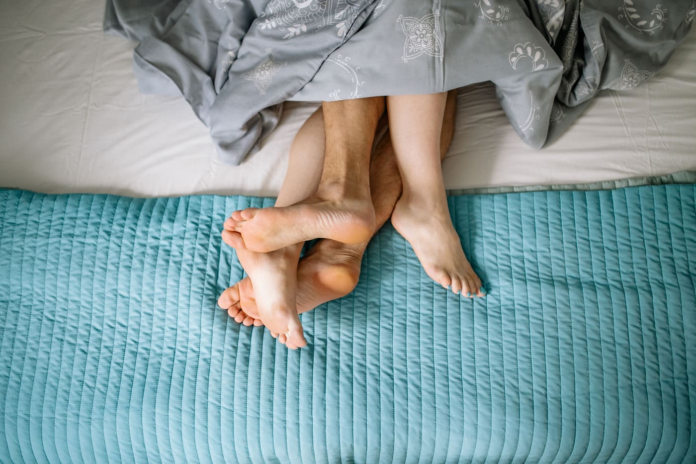 Close-up of a couple's bare feet tangled together under the covers