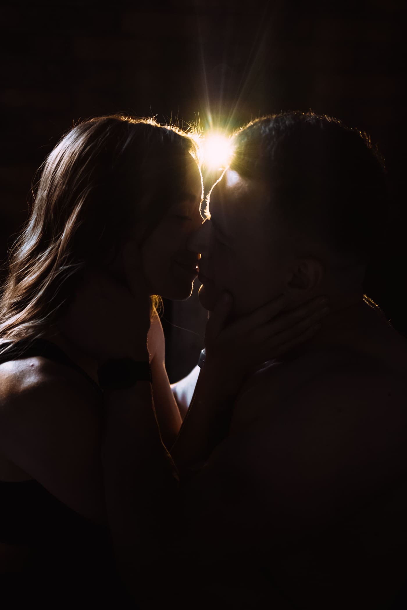 Silhouette of a couple almost kissing, backlit in a dark room at night
