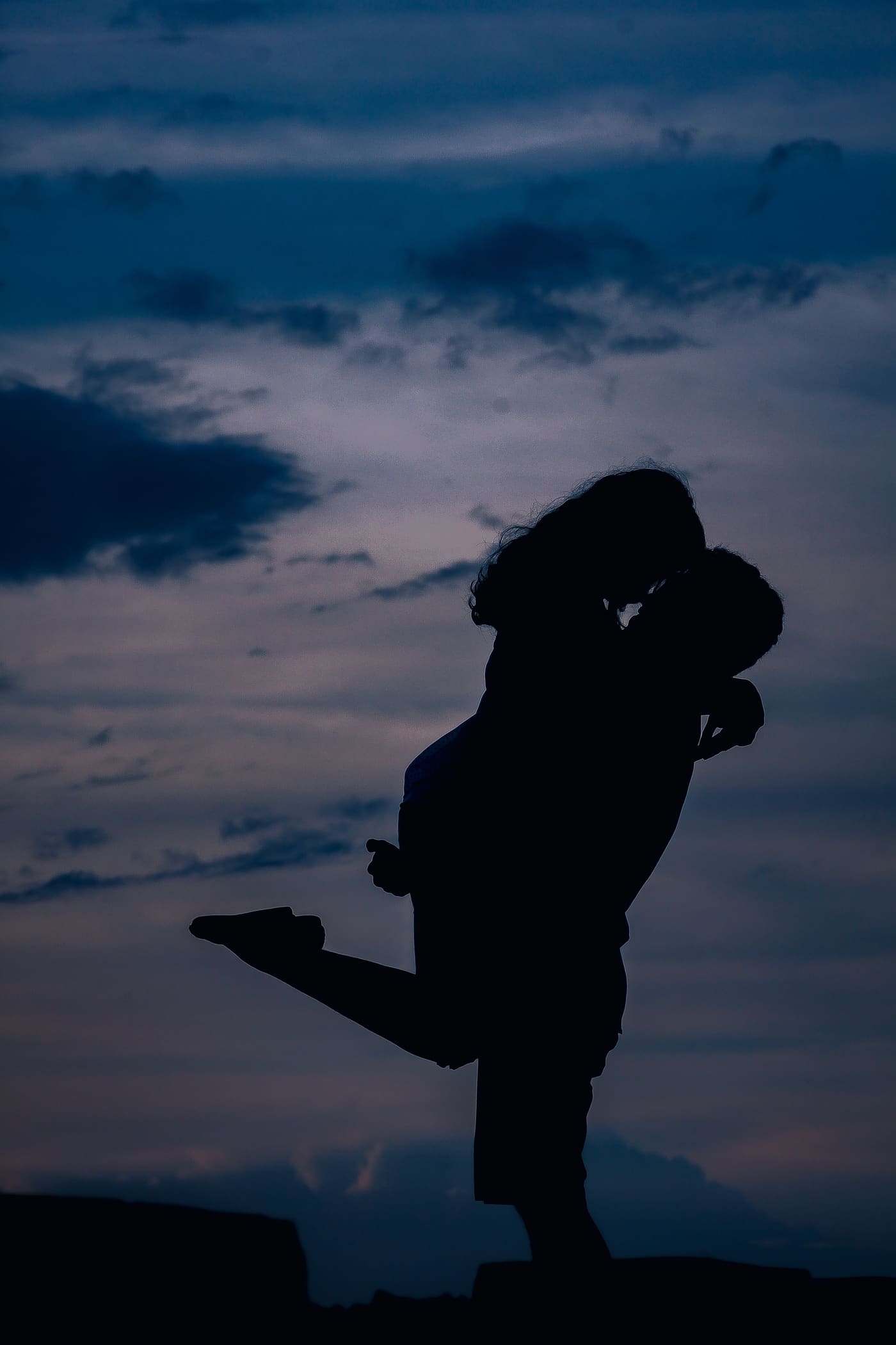 Silhouette of a couple in a playful embrace against a dusk sky
