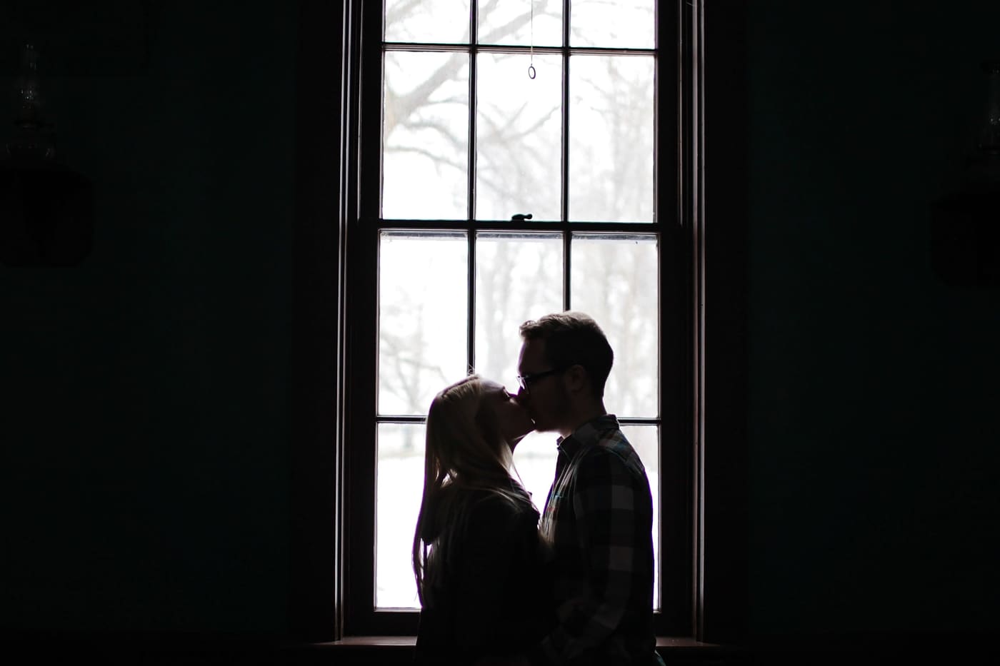 Silhouette of a couple kissing in front of a bright window